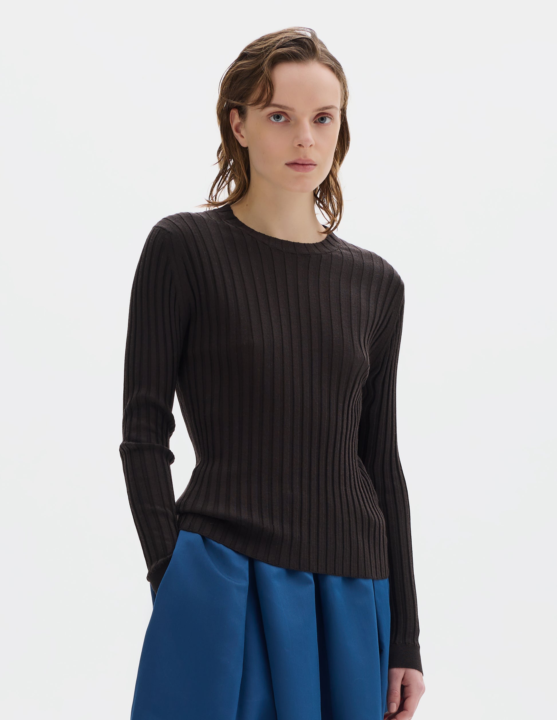 Cropped body image, front view of model wearing neat fitting dark brown merino top with wide rib through body, wide contrast rib on crew neck, and set-in long sleeves with fine rib cuffs. Styled with blue skirt.
