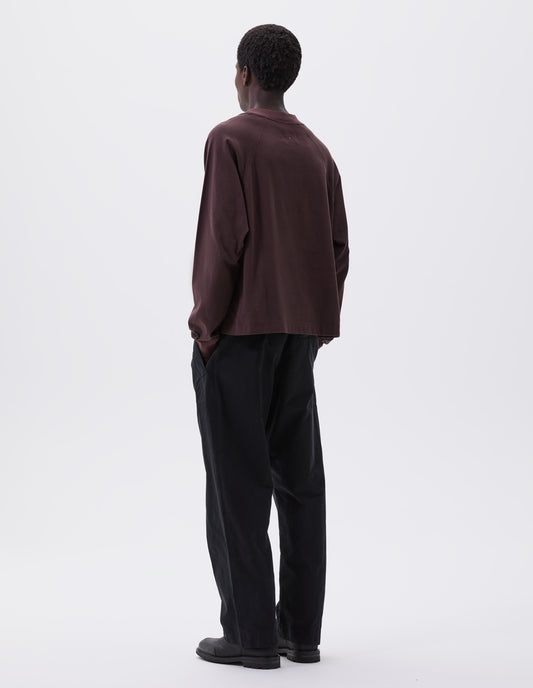 Full body image, back view of model wearing relaxed black trousers with slant welt pockets  and press stud hem adjusters. Styled with brown long sleeve t-shirt and black leather boots. 