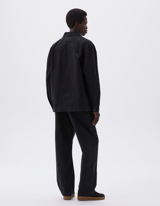 Full body image, back view of model wearing black overshirt with adjustable cuffs and vent split hem. Styled with matching black trousers and black suede t-shirt. 
