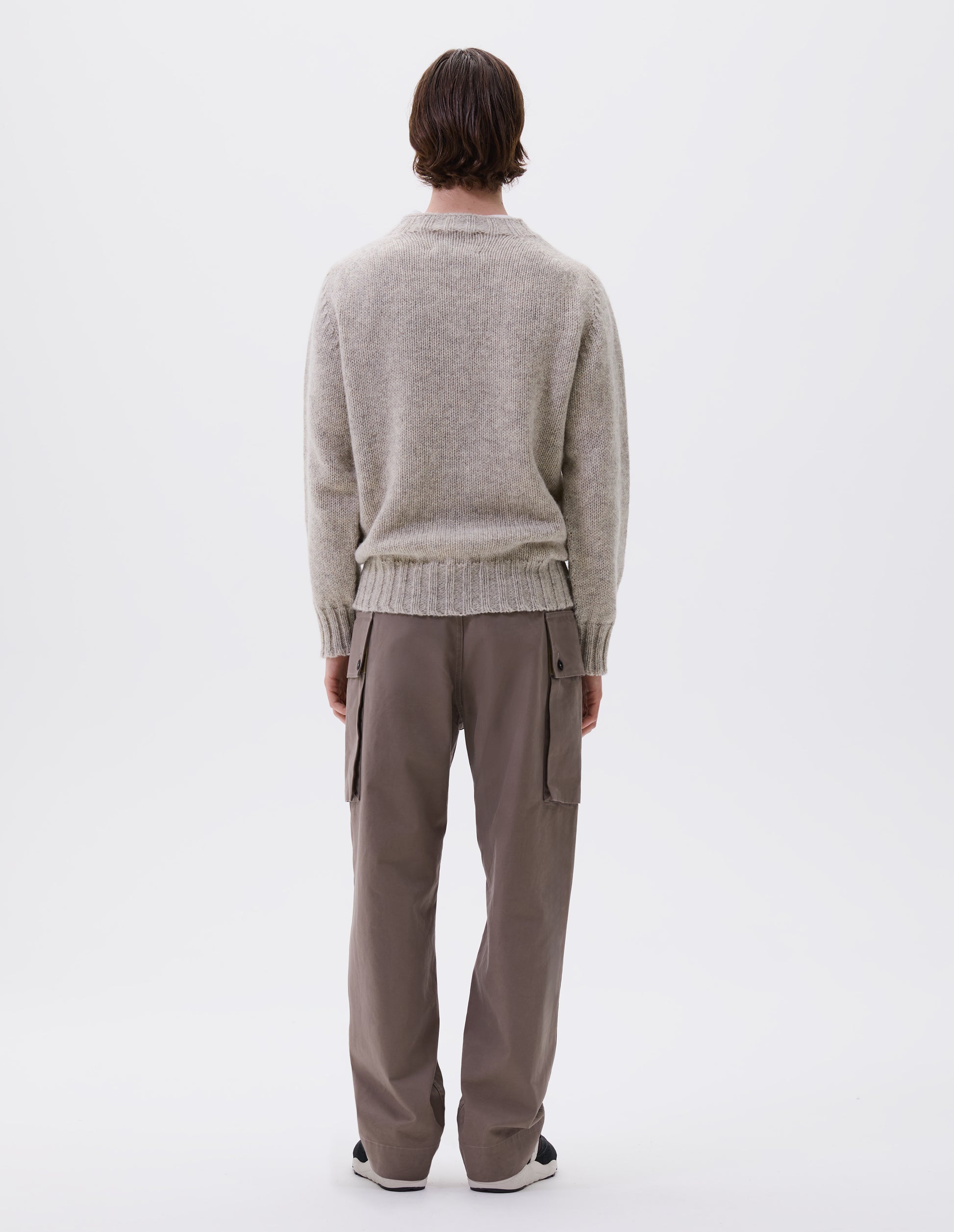 Full body image, back view of model wearing beige marl jumper with saddle sleeves and contrasting rib on neck, cuffs and hem. Styled with beige trousers and black and brown trainers.