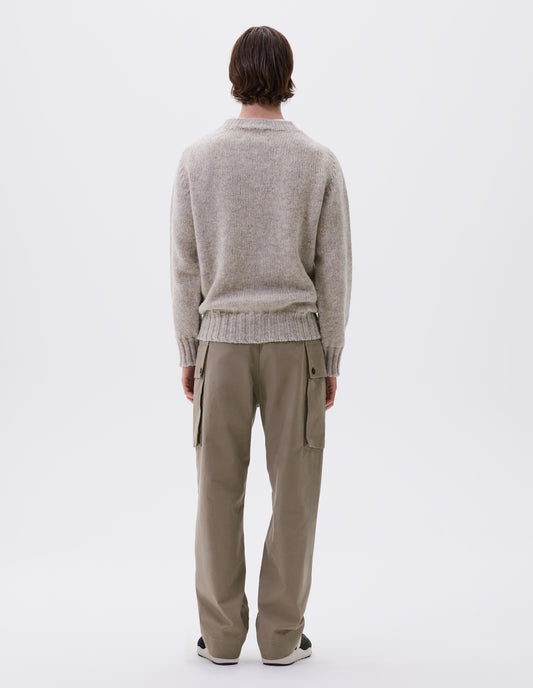 Full body image, back view of model wearing beige cargo trousers with deep flap button fastening patch pocket, belt loops and welt pocket on back yoke. Styled with beige jumper and brown and black trainers.
