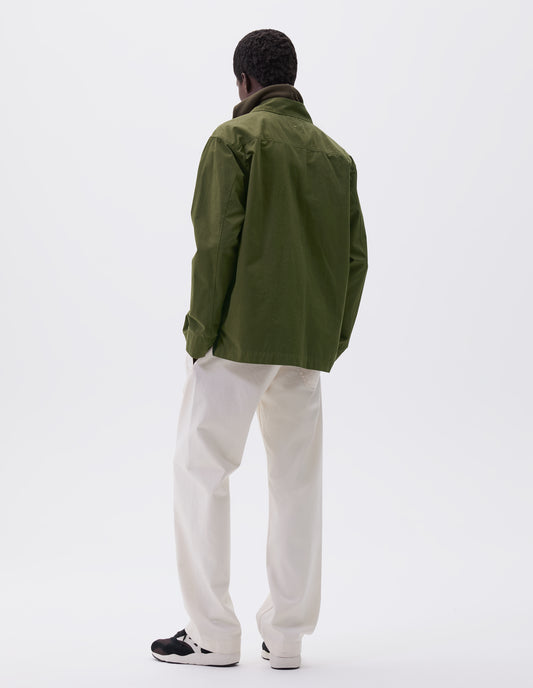 Full body image, back view of model wearing relaxed, overshirt cut green shirt with straight cuffs and vent split hem with herringbone tape detailing. Styled over green hoodie, white trousers and black, brown and white trainers.