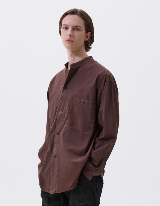 Cropped body image, front view of model wearing brownish red cotton collarless shirt, with stitch through placket, button-through patch pocket and curved side gusset. Styled with black denim jeans.
