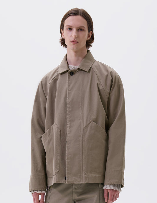Cropped body image, front view of model wearing beige raglan sleeve jacket with corozo button fastening fly front and slant patch pockets. Styled over a chunky beige jumper, with matching trousers.