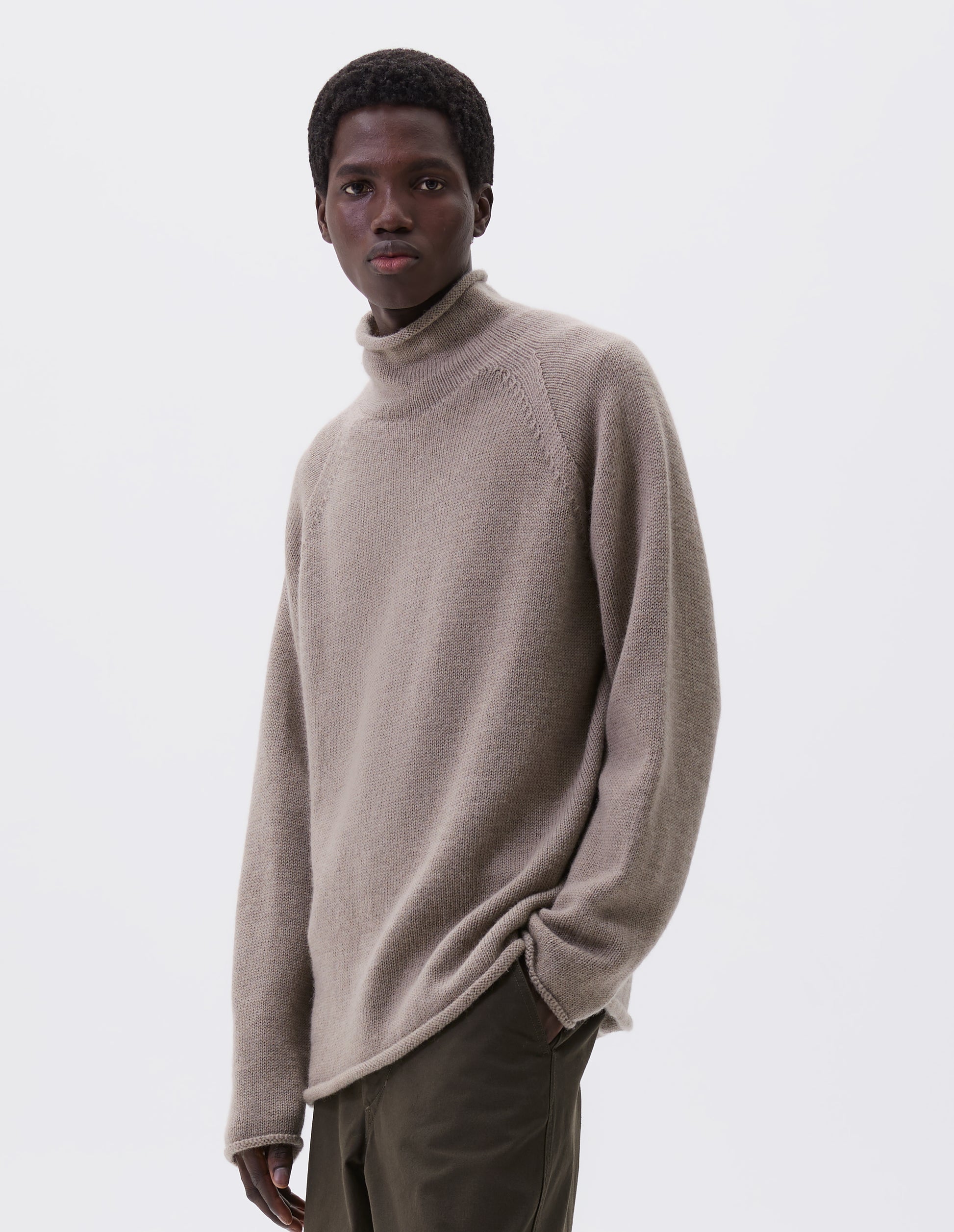 Cropped body image, front view of model wearing beige roll neck jumper with seamless construction, high neck, raglan sleeve and straight cuffs and hem. Styled with green trousers.