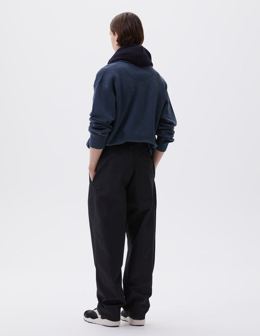 Full body image, back view of model wearing black heavy cotton trousers, with belt loops and stitch through back pocket. Styled with blue knitted polo, navy blue knitted hood and black and brown trainers. 