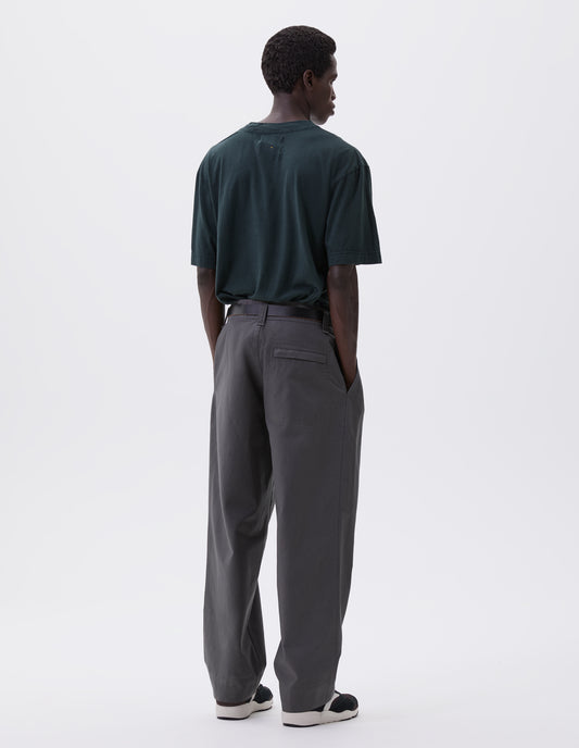 Full body image, back view of model wearing charcoal grey heavy cotton trousers with belt loops and stitch through back pocket. Styled with blue t-shirt, black leather belt and black and brown trainers.