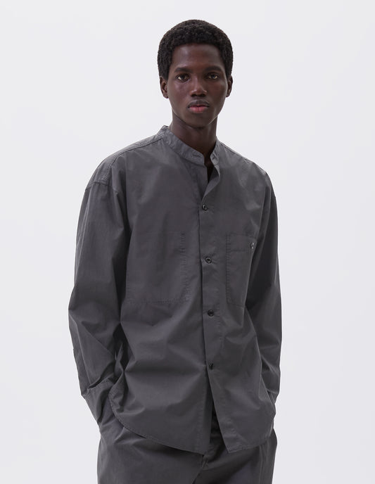Cropped body image, front view of model wearing dark grey cotton collarless shirt, with stitch through placket, button-through patch pocket and curved side gusset. Styled with grey trousers.