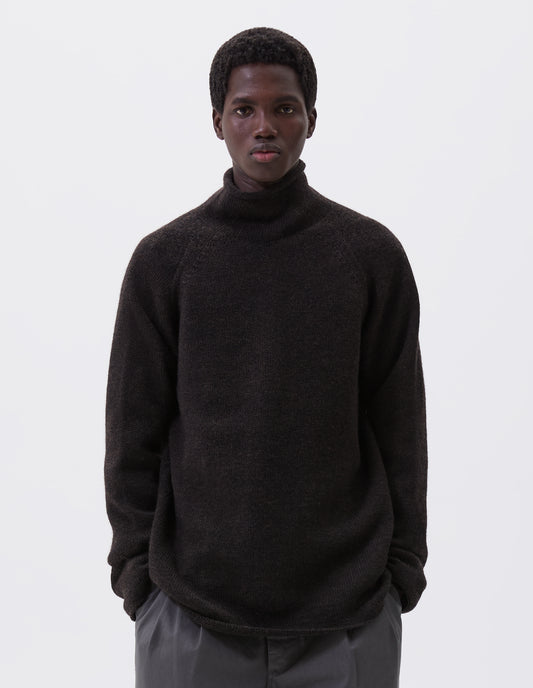 Cropped body image, front view of model wearing brown roll neck jumper with seamless construction, high neck, raglan sleeve and straight cuffs and hem. Styled with grey trousers.
