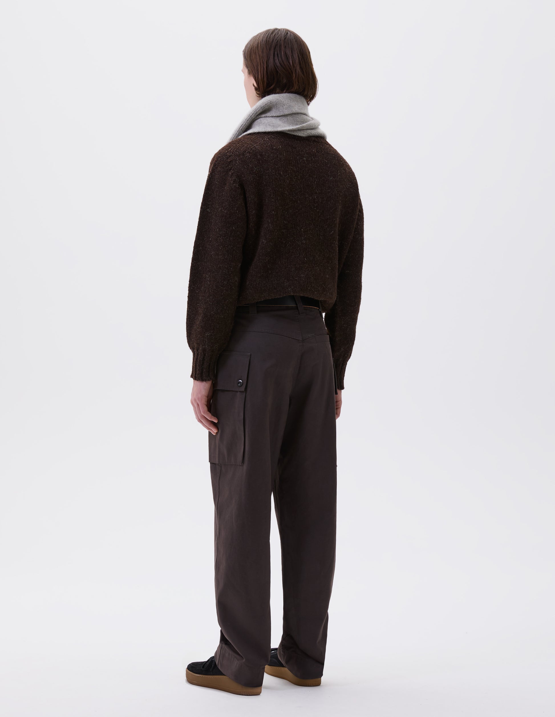 Full body image, back view of model wearing brown cargo trousers with deep flap button fastening patch pocket, belt loops and welt pocket on back yoke. Styled with brown jumper, grey scarf, black leather belt and black suede trainers.