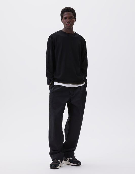 Full body image, front view of model wearing black long sleeve knitted thermal with ribbed collar, khaki green stripe on cuffs and hem, styled with thermal over white t-shirt, black trousers and black, brown and white trainers. 