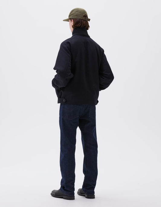 Full body image, front view of model wearing indigo denim twill jeans, with metal button fly, grown on waistband with belt loops and back pockets with half cotton lining. Styled with green cap, navy blue jacket and black leather boots.