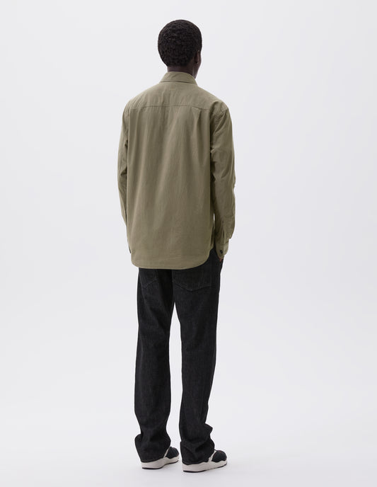 Full body image, back view of model wearing green brushed cotton shirt with side gusset stitch detailing and pleated back yoke. Styled with black denim jeans and black and brown trainers.