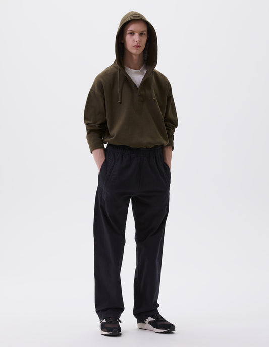 Full body image, front view of model wearing relaxed dark blue joggers with elasticated waist and deep welt pockets. Styled with white t-shirt, green hoodie and black, brown and white trainers.