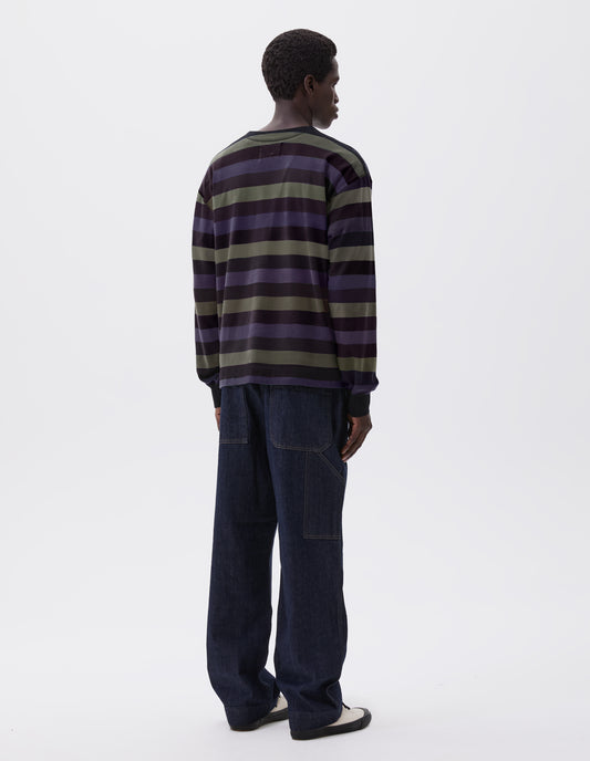Full body image, back view of model wearing off black, blue and green striped long sleeve t-shirt, with single rib cuff and self faced neck. Styled with indigo blue jeans and ecru canvas trainers. 