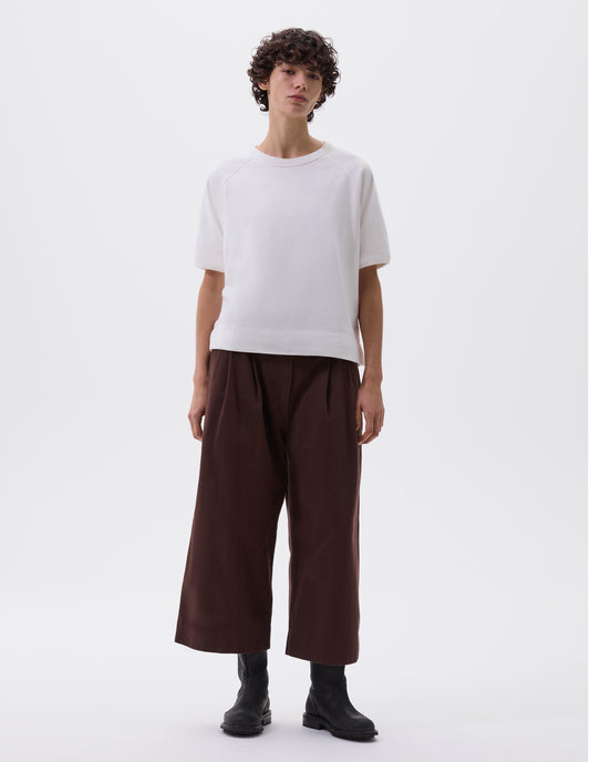 Full body image, front view of model wearing white t-shirt with raglan sleeves and ribbed binding on neckline and cuffs, styled with dark purple cropped trousers and black leather biker boots.