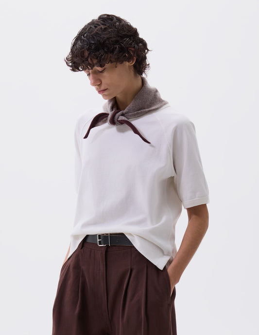 Cropped body image, front view of female model wearing beige wool scout scarf with dark red wool trim. Styled with white t-shirt, black leather belt and burgundy pleated trousers.