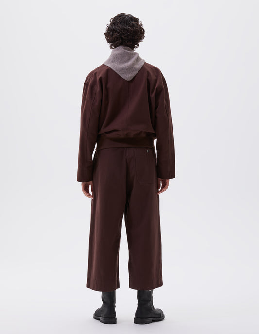Full body image, back view of model wearing red brown collared jacket with ribbed hem. Styled with matching culottes, grey knitted scout scarf and black leather boots. 