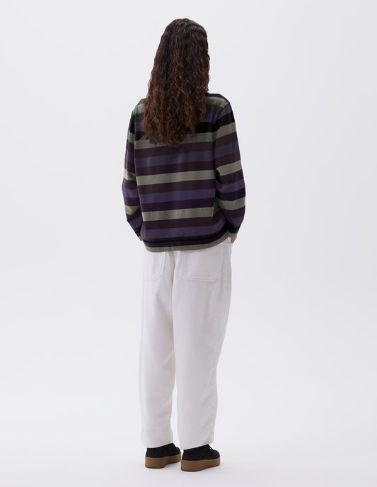 Full body image, back view of model wearing off black, blue and green striped long sleeve top, with contrast rib neck. Styled with white corduroy trousers and black nubuck leather trainers. 