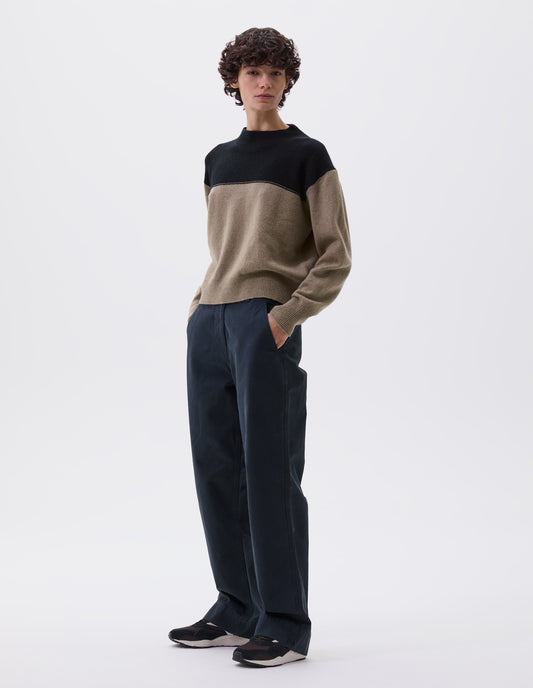 Full body image, front view of model wearing cropped black and beige jumper with ribbed crew neck, cuffs and hem. Styled with black trousers and black, brown and white trainers.
