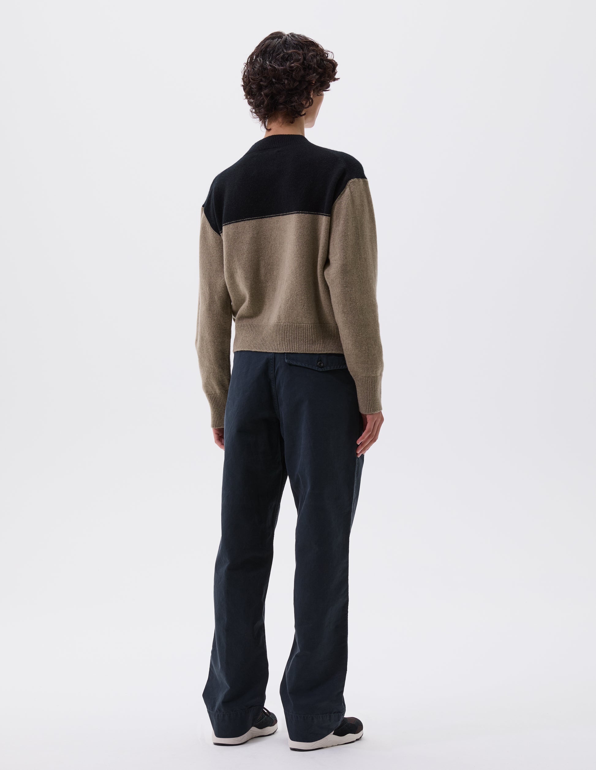 Full body image, back view of model wearing cropped black and beige jumper with ribbed crew neck, cuffs and hem. Styled with black trousers and black, brown and white trainers.