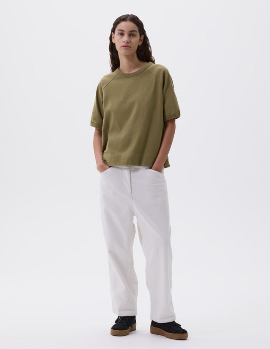 Full body image, front view of model wearing light green t-shirt with raglan sleeves and ribbed binding on neckline and cuffs, styled with white trousers and black nubuck trainers.