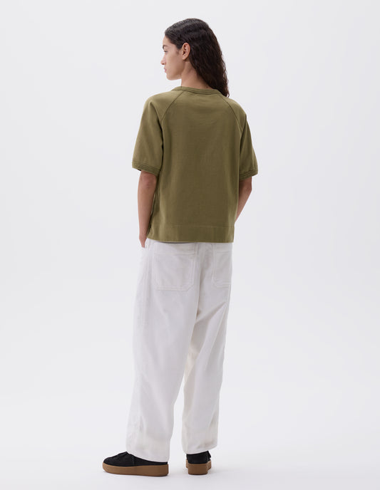 Full body image, back view of view of model wearing light green t-shirt with raglan sleeves and ribbed binding on neckline and cuffs, styled with white trousers and black nubuck trainers.
