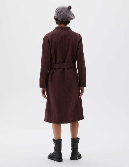 Full body image, back view of model wearing brown red long sleeve shirt dress, with patch back pocket, corozo button fastening cuffs and removeable belt.  Styled with grey bobble hat and black leather boots.