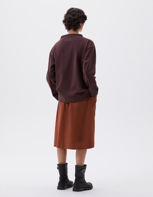 Full body image, back view of model wearing dark brown smock neck long sleeve t-shirt. Styled with dark orange skirt and black leather biker boots.