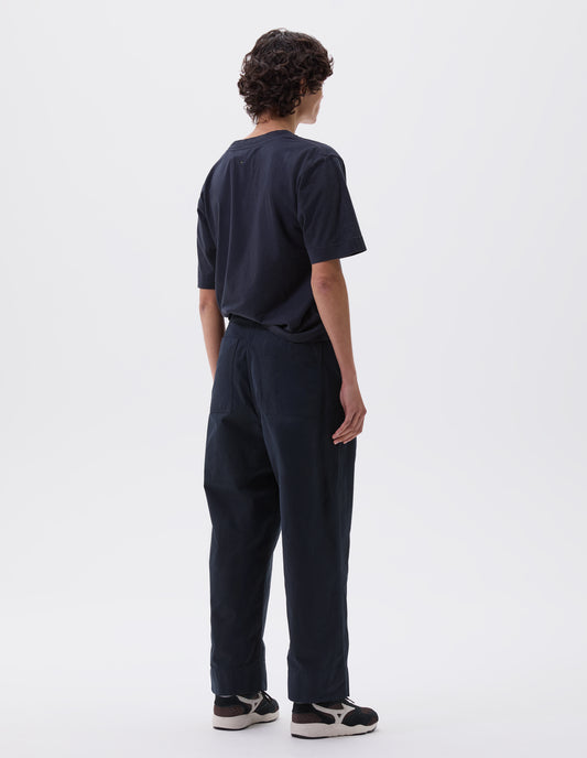 Full body image, back view of model wearing navy blue trousers with  patch back pockets and deep stitch hem. Styled with navy blue t-shirt and black and brown trainers.