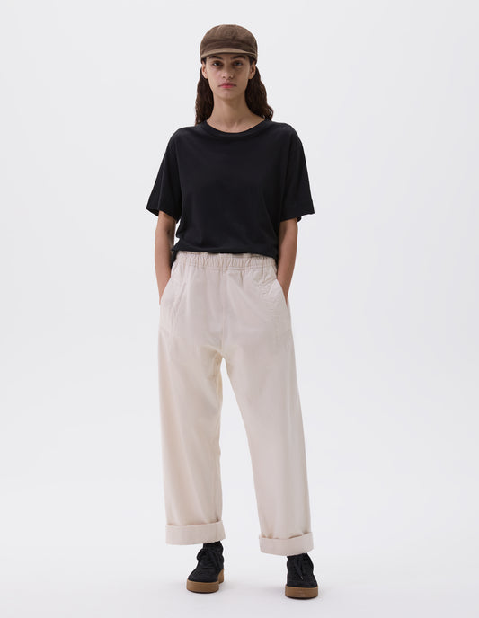 Full body image, front view of model wearing relaxed white joggers with elasticated waist and deep welt pockets. Styled with khaki green cap, black t-shirt and black nubuck trainers.