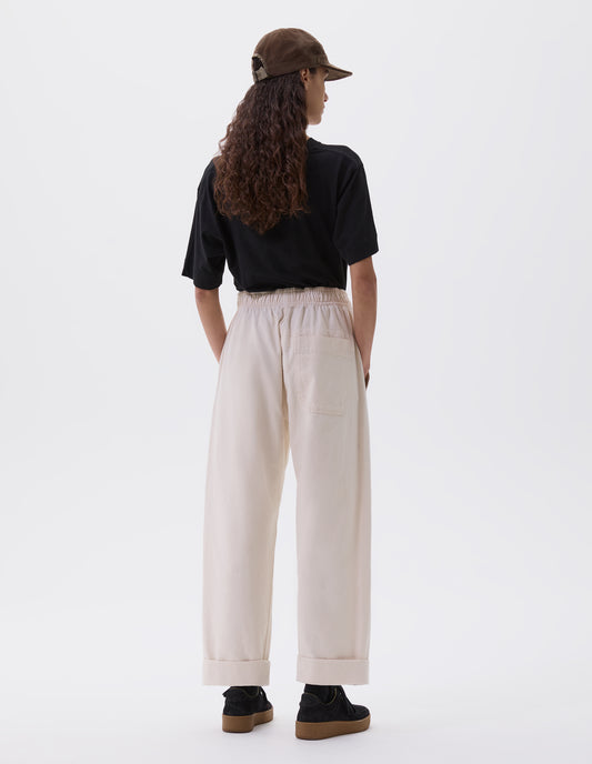 Full body image, back view of model wearing relaxed white joggers with elasticated waist and patch back pocket. Styled with khaki green cap, black t-shirt and black nubuck trainers.