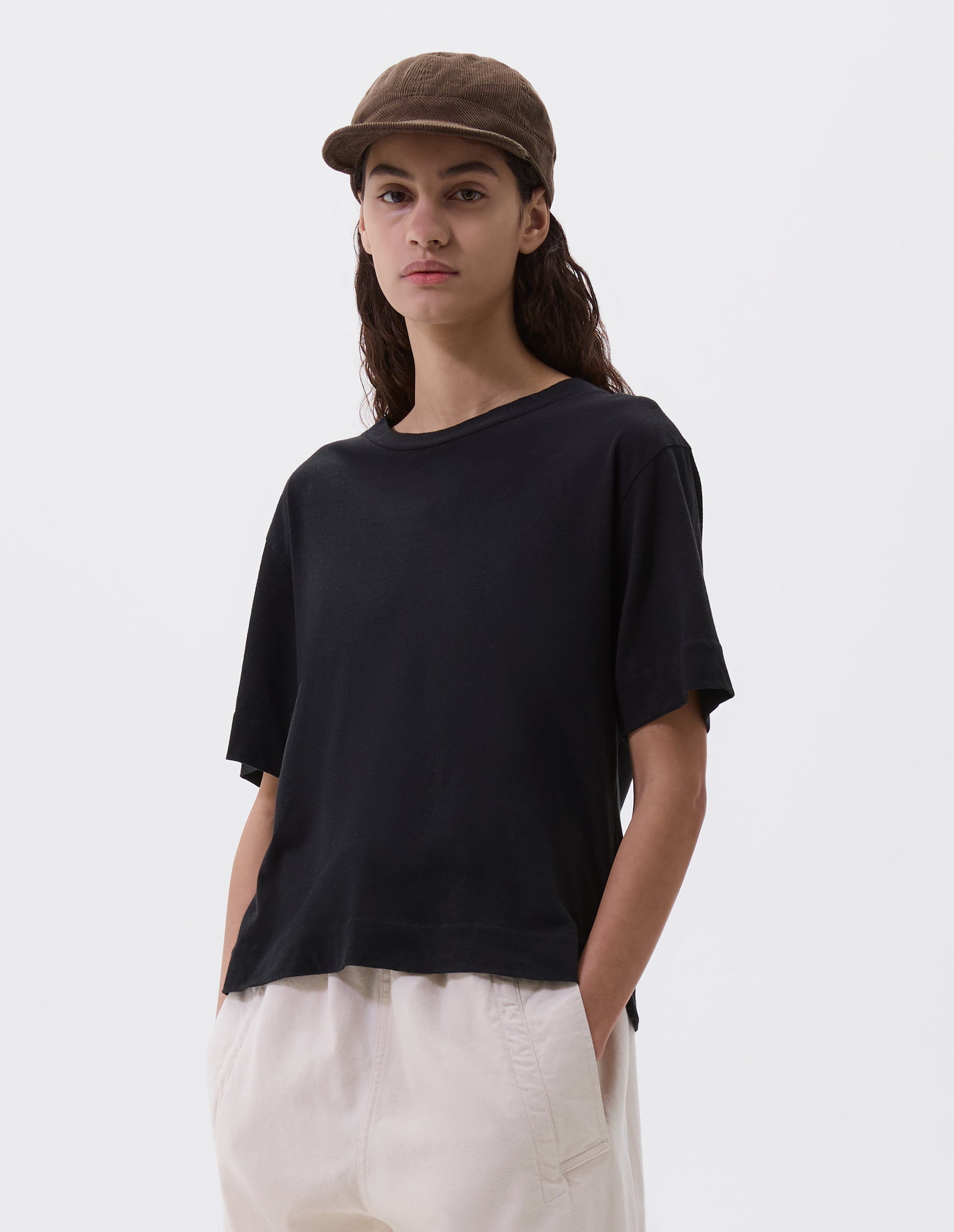 Cropped body image, front view of female model wearing khaki beige corduroy cap. Styled with black t-shirt and off white trousers.