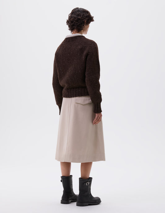 Full body image, back view of model wearing dark brown rustic wool jumper with saddle sleeve and contrasting rib on neck, cuffs and hem. Styled with beige skirt and black leather boots.