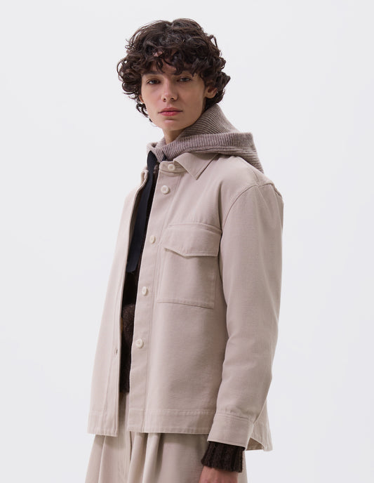 Cropped body image, front view of female model wearing beige knitted wool hood with contrasting black herringbone tape to adjust and contrast rib on face. Styled with beige jacket and matching skirt.