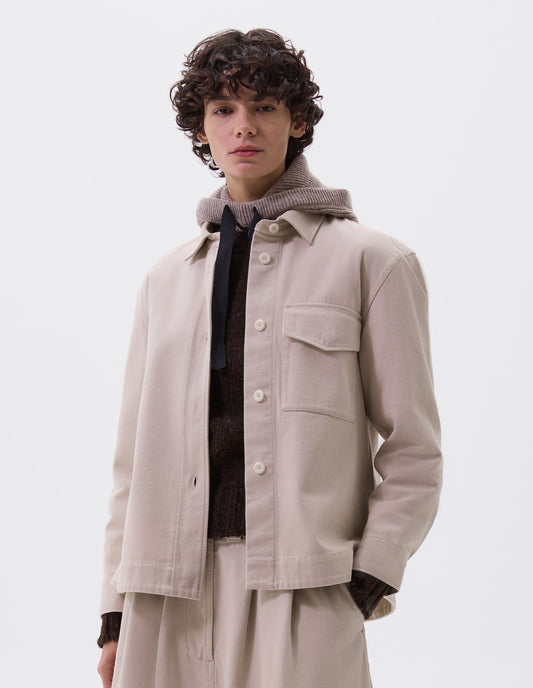 Cropped body image, front view of model wearing beige oversized shirt with stitch through raised placket, corozo button fastening, patch chest pocket and deep stitch hem. Styled with matching skirt, brown jumper and beige hooded scarf.