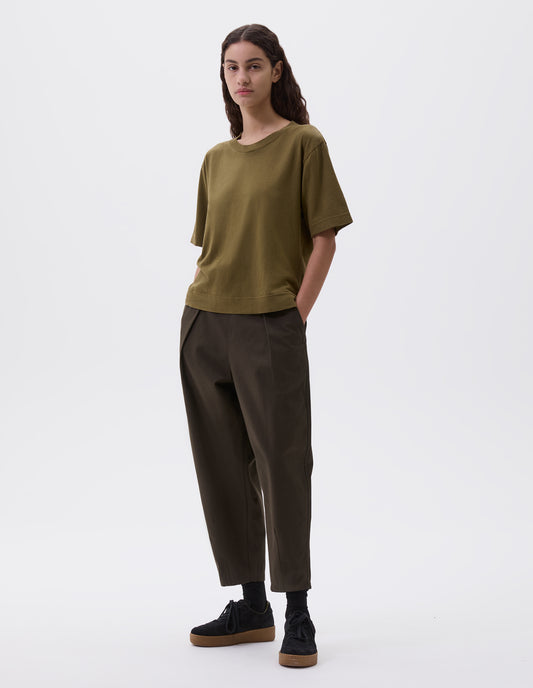 Full body image, front view of model wearing green boxy t-shirt. Styled with cropped dark brown trousers with side pockets, black socks and black nubuck trainers. 