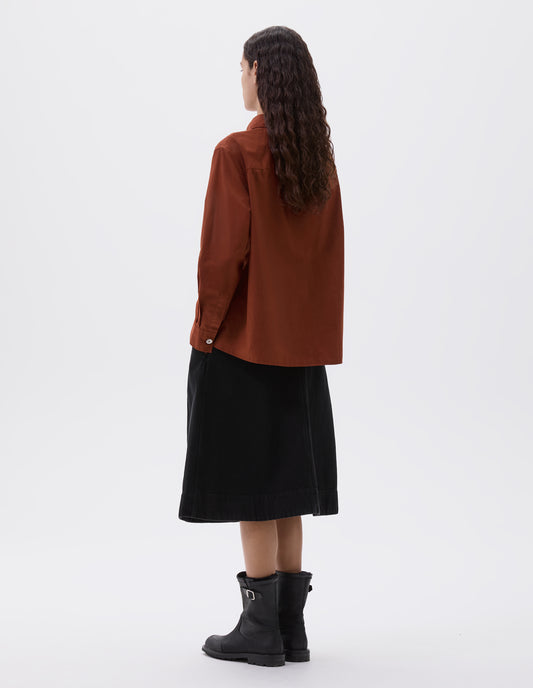 Full body image, back view of model wearing brownish red shirt with corozo button cuffs. Styled with black denim skirt and black leather boots.