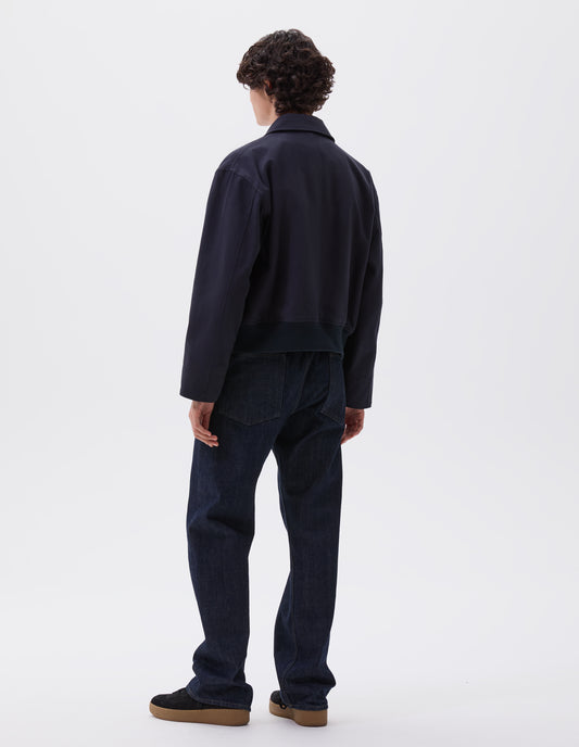 Full body image, back view of model wearing dark navy collared jacket with ribbed hem. Styled with indigo blue denim jeans and black nubuck trainers. 
