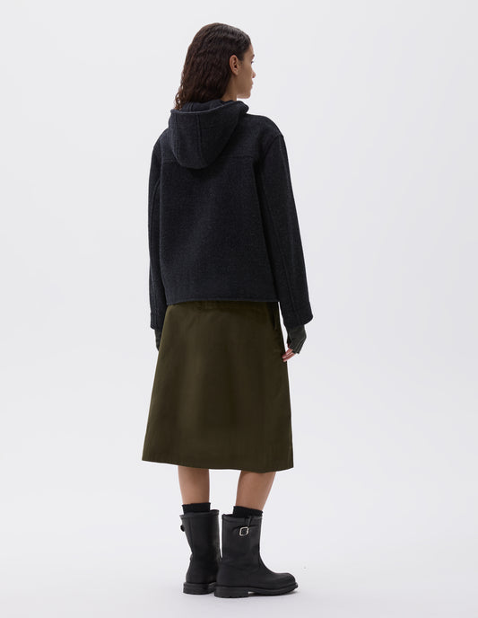 Full body image, back view of model wearing charcoal grey short hooded duffle coat, with back yoke detailing. Styled with brown fingerless gloves, olive green skirt, black socks and black leather boots.