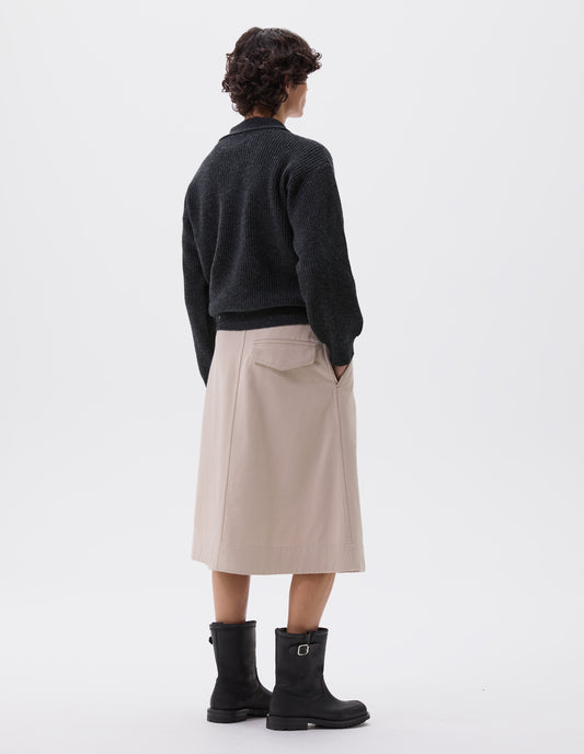 Full body image, back view of model wearing dark grey knitted polo with  contrast rib on collar and cuffs. Styled with beige midi skirt with side pockets and black leather biker boots.