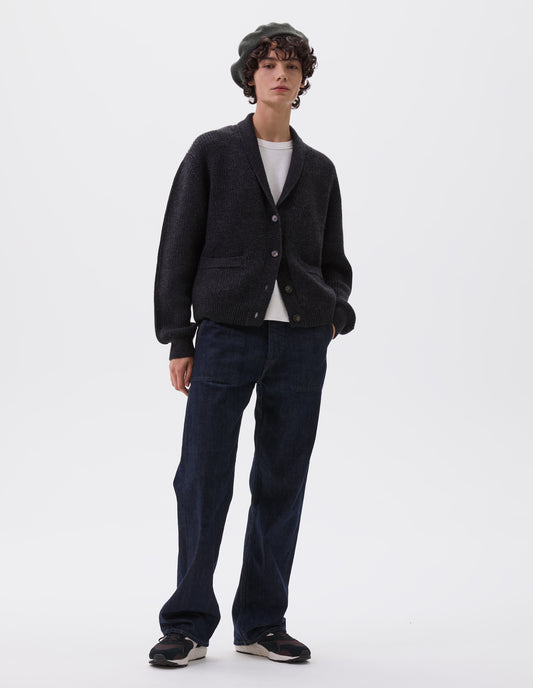 Full body image, front view of model wearing dark grey cardigan with ribbed collar, cuffs and hem, patch pockets and corozo brace buttons. Styled over white t-shirt, dark blue jeans, dark green beret and black, brown and white trainers.