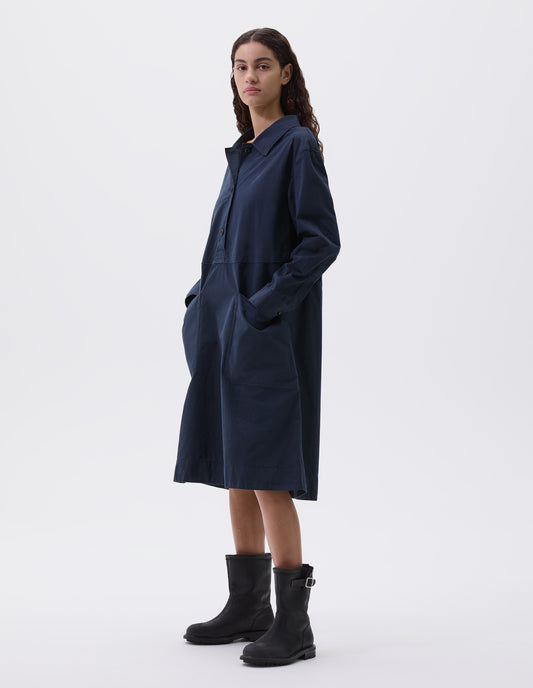 Full body image, front view of model wearing dark blue long sleeve shirt dress with box stitch detailing, large apron patch pockets, deep stitch hem and waist seam detail. Styled with black leather biker boots.