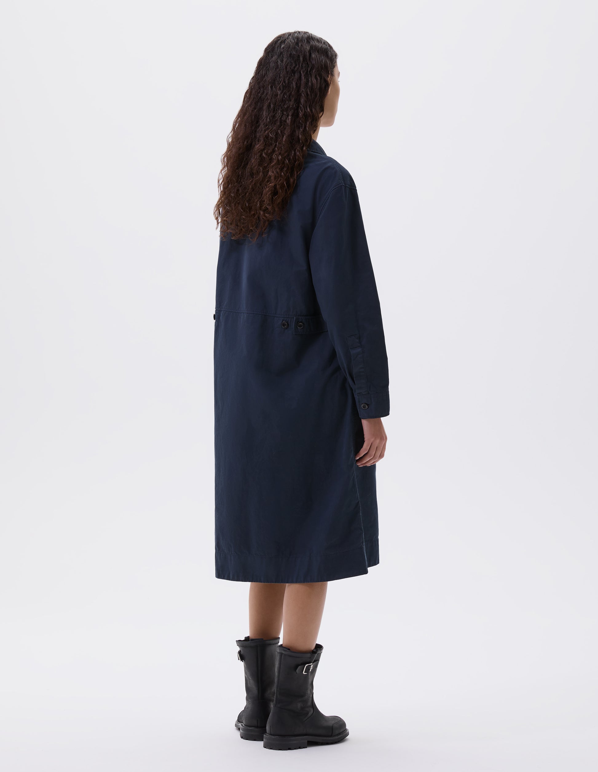 Full body image, back view of model wearing dark blue long sleeve shirt dress with deep stitch hem and waist seam detail with button tab adjusters. Styled with black leather biker boots.