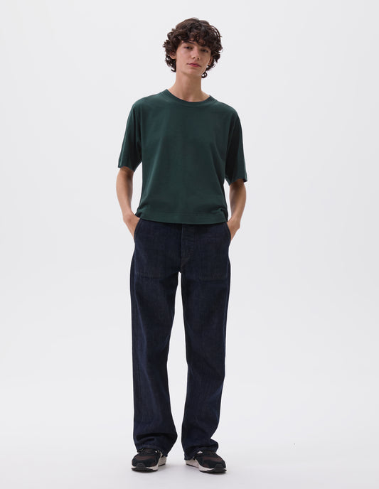 Full body image, front view of model wearing blue green boxy t-shirt. Styled with dark blue jeans and black, brown and white trainers.