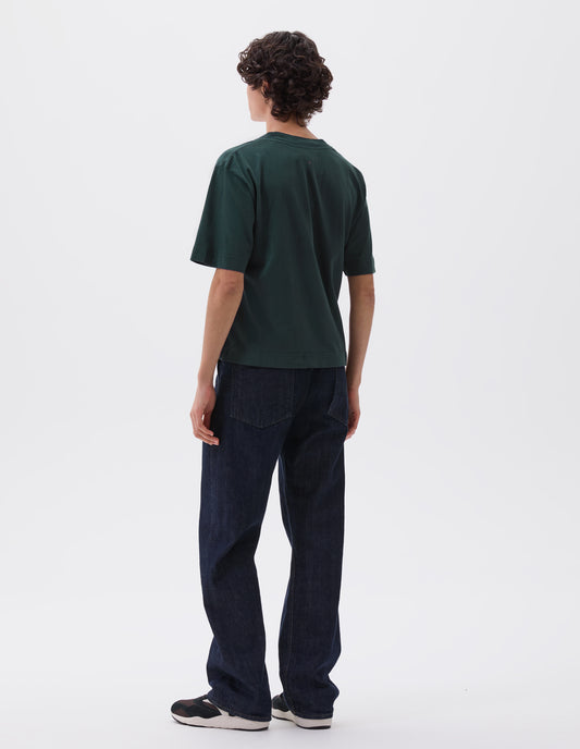 Full body image, back view of model wearing blue green boxy t-shirt. Styled with dark blue jeans and black, brown and white trainers.