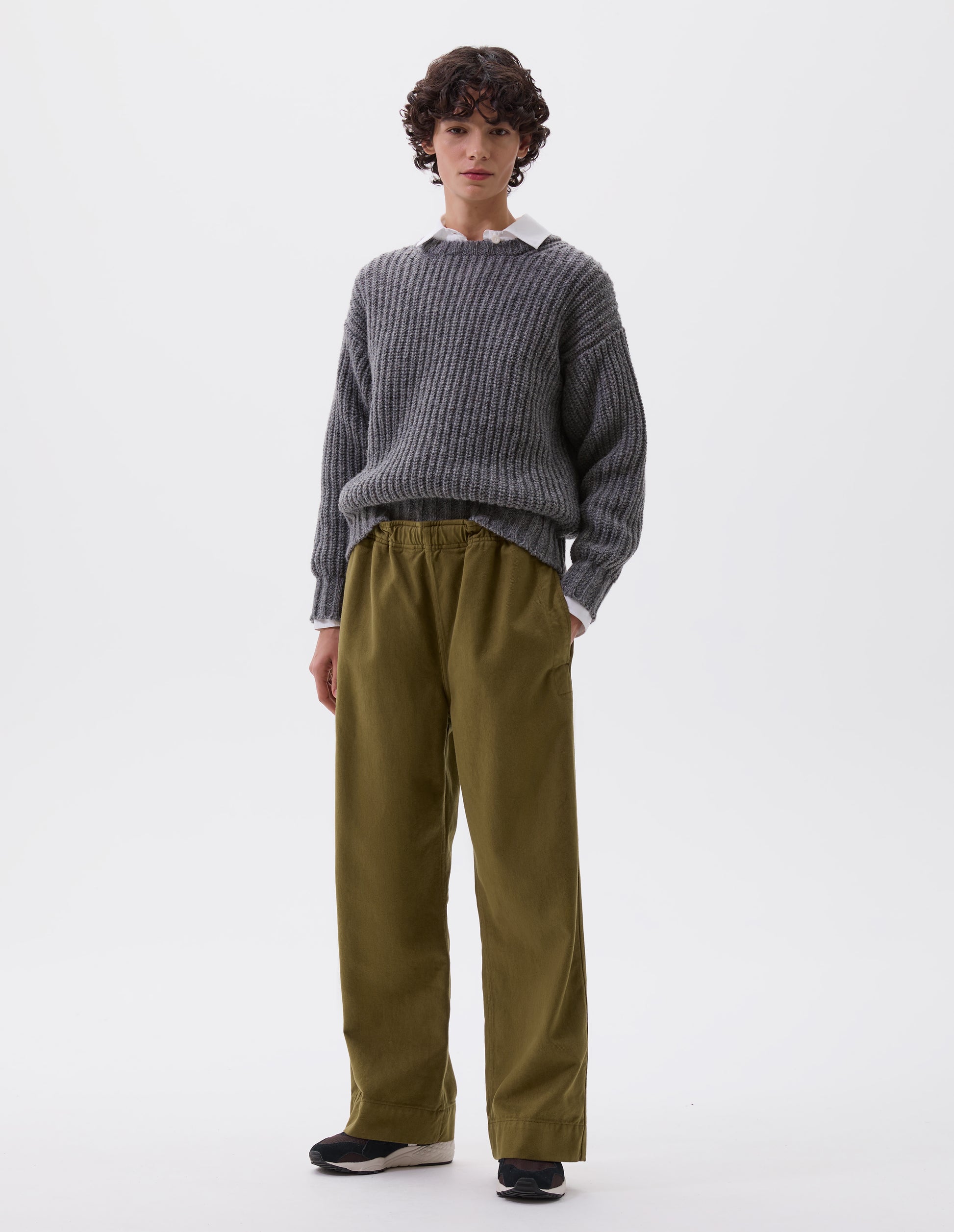 Full body image, front view of model wearing green relaxed wide leg joggers with elasticated waistband and side seam pockets. Styled with grey jumper over white shirt and black, brown and white trainers.