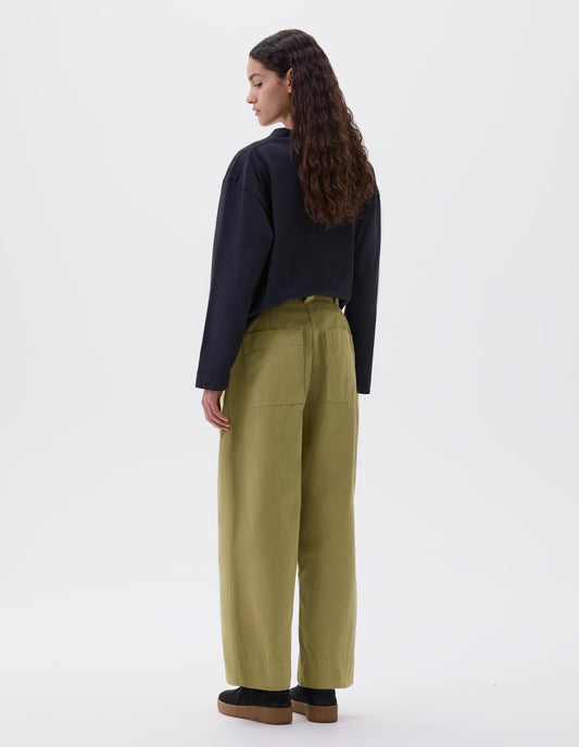 Full body image, back view of model wearing green trousers with  patch back pockets and deep stitch hem. Styled with navy blue long sleeve top and black suede trainers.