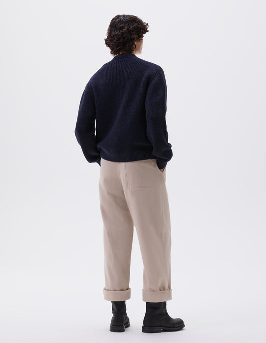Full body image, back view of model wearing dark blue cardigan with ribbed collar, cuffs and hem. Styled with beige trousers and black leather biker boots.