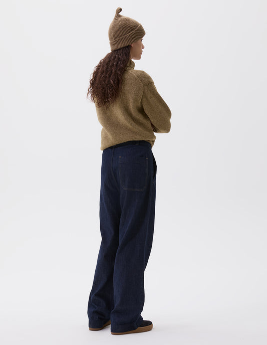 Full body image, back view of model wearing indigo blue wide leg light denim twill jeans. With slant side pockets and patch back pocket. Styled with yellowy green high neck jumper and matching hat, with black nubuck leather trainers.